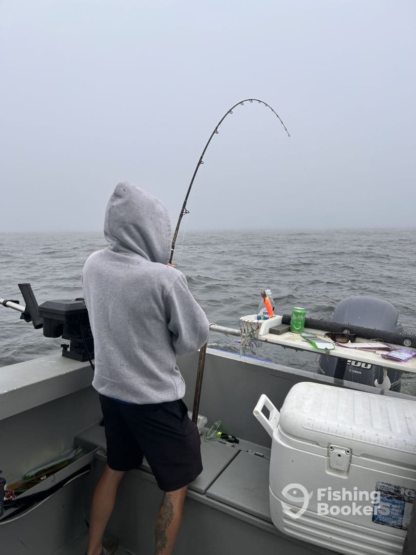 Angler reeling in a catch on a foggy day while fishing from a boat, showcasing the excitement of the sport.