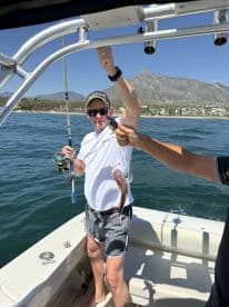 Angler reeling in a catch while enjoying a sunny day on the water, with scenic mountains in the background.
