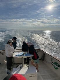 A group of young anglers enjoying a day on the water aboard a fishing boat, with a scenic view of the ocean and sky.