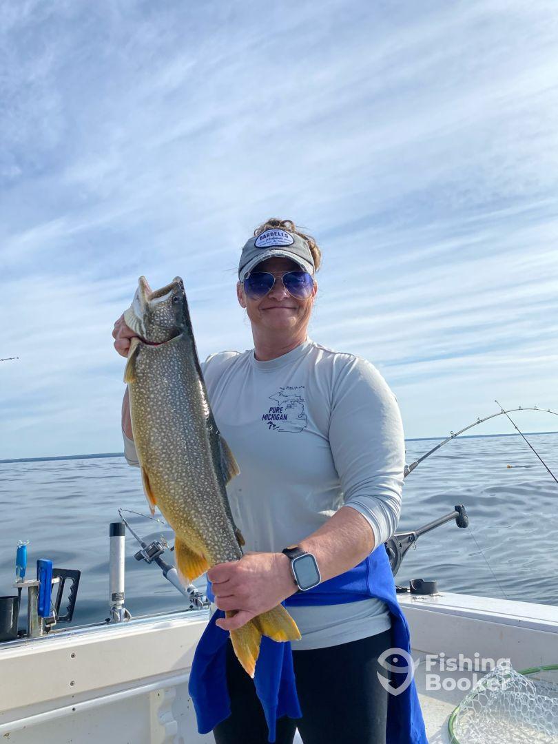 An angler proudly displaying a large Lake Trout while fishing on a boat in Michigan's waters.