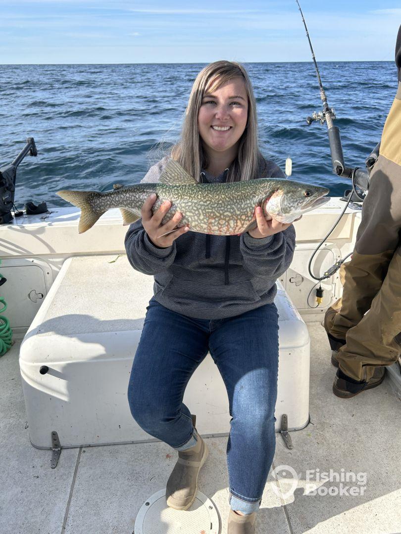A happy angler displaying a beautiful Lake Trout while fishing on a boat in open waters.