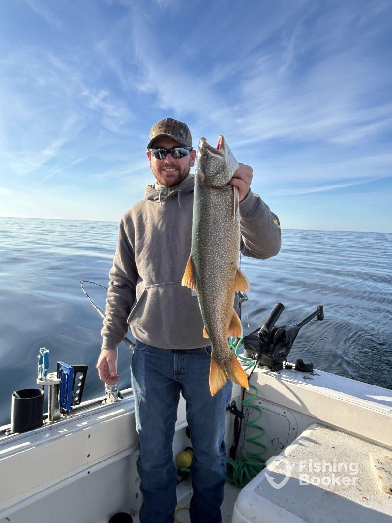 An angler proudly displaying a large Lake Trout while fishing on a calm lake, showcasing a successful day on the water.