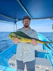 Angler proudly displaying a vibrant Mahi-Mahi aboard a fishing boat in clear blue waters.