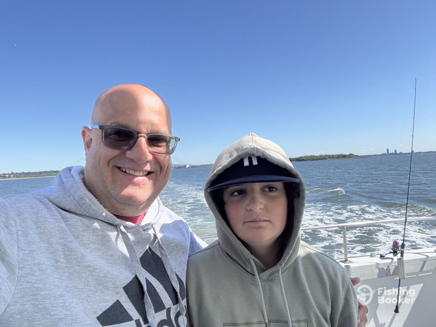 A father and son enjoying a day of fishing on a boat, with a scenic water view in the background.