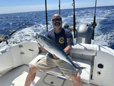 An angler proudly displaying a large King Mackerel while fishing offshore, showcasing a successful day on the water.