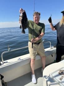 An angler proudly displaying a large Black Sea Bass while fishing on a calm day at sea.