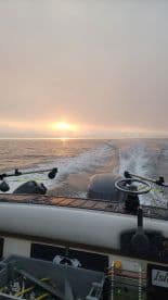 A scenic view from the boat as it cuts through calm waters during sunset, showcasing the helm and fishing gear.