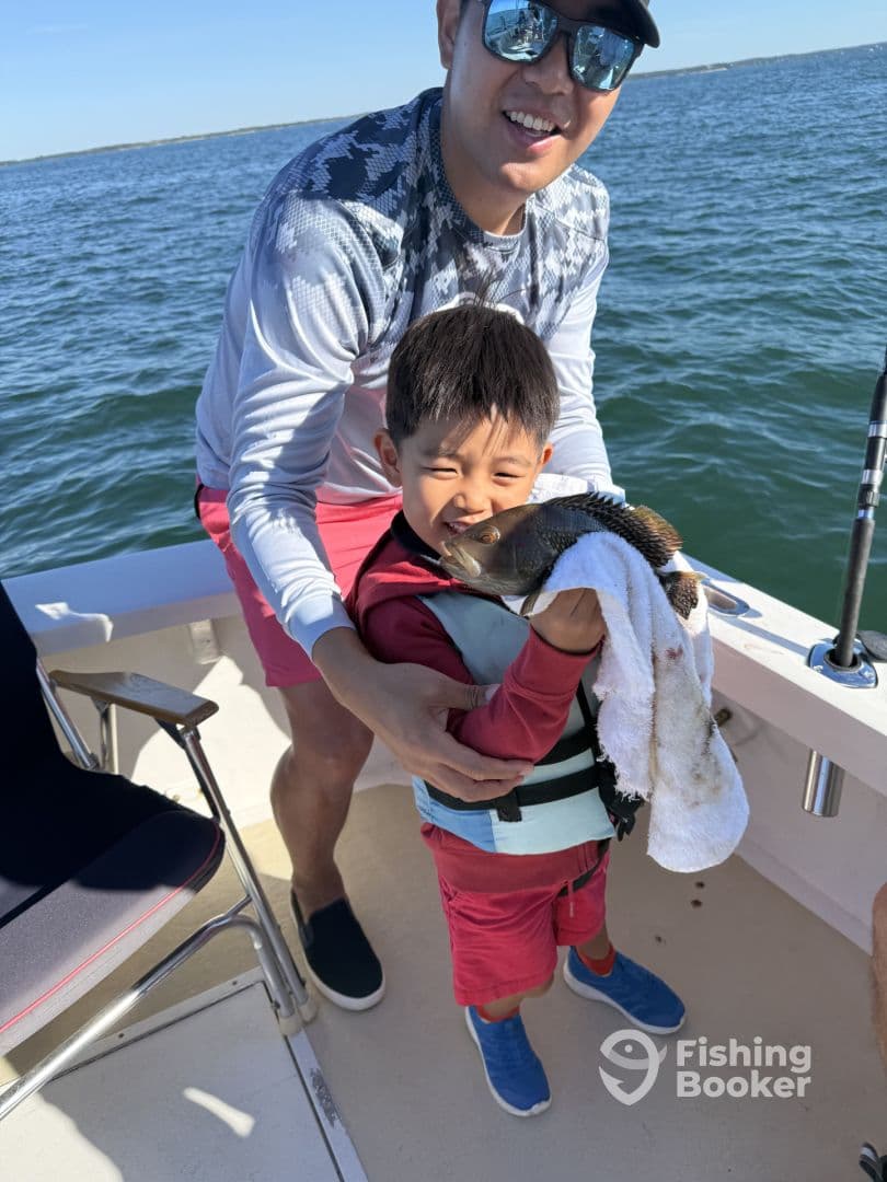 A young boy proudly holding a fish with the help of an adult on a fishing boat, showcasing a memorable moment on the water.