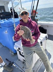 An angler proudly displaying a Flounder while fishing on a charter boat, surrounded by fellow fishermen.