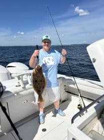 Angler proudly displaying a large Flounder while fishing on a boat in open waters.