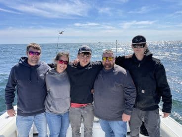 A group of anglers posing together on a boat, enjoying a day out on the water. The bright sun and ocean backdrop create a vibrant atmosphere.