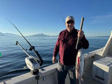An angler proudly displaying a freshly caught fish while on a boat in calm waters, surrounded by mountains in the background.