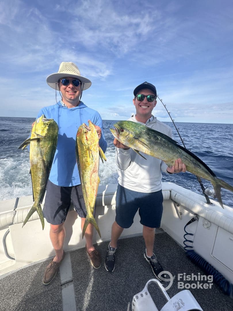 Two anglers proudly displaying their catch of Mahi Mahi while aboard a fishing boat in open waters.