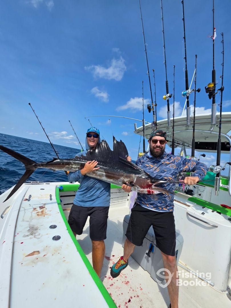 Two anglers proudly displaying a large Sailfish on a sport fishing boat, showcasing a successful deep-sea fishing trip.