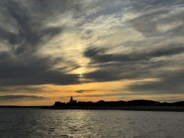 A scenic view of a lighthouse against a dramatic sunset, capturing the tranquil atmosphere of the fishing environment.