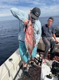 A young angler proudly displaying a large Red Snapper on a fishing boat, showcasing a successful offshore fishing trip.