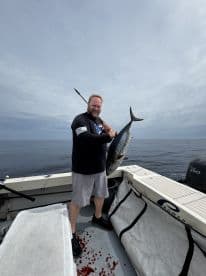 An angler proudly displaying a large tuna on a fishing boat, showcasing a successful deep-sea fishing trip.