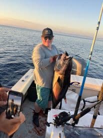 A proud angler holding a large tuna on a fishing boat during a sunset trip, showcasing the excitement of deep-sea fishing.