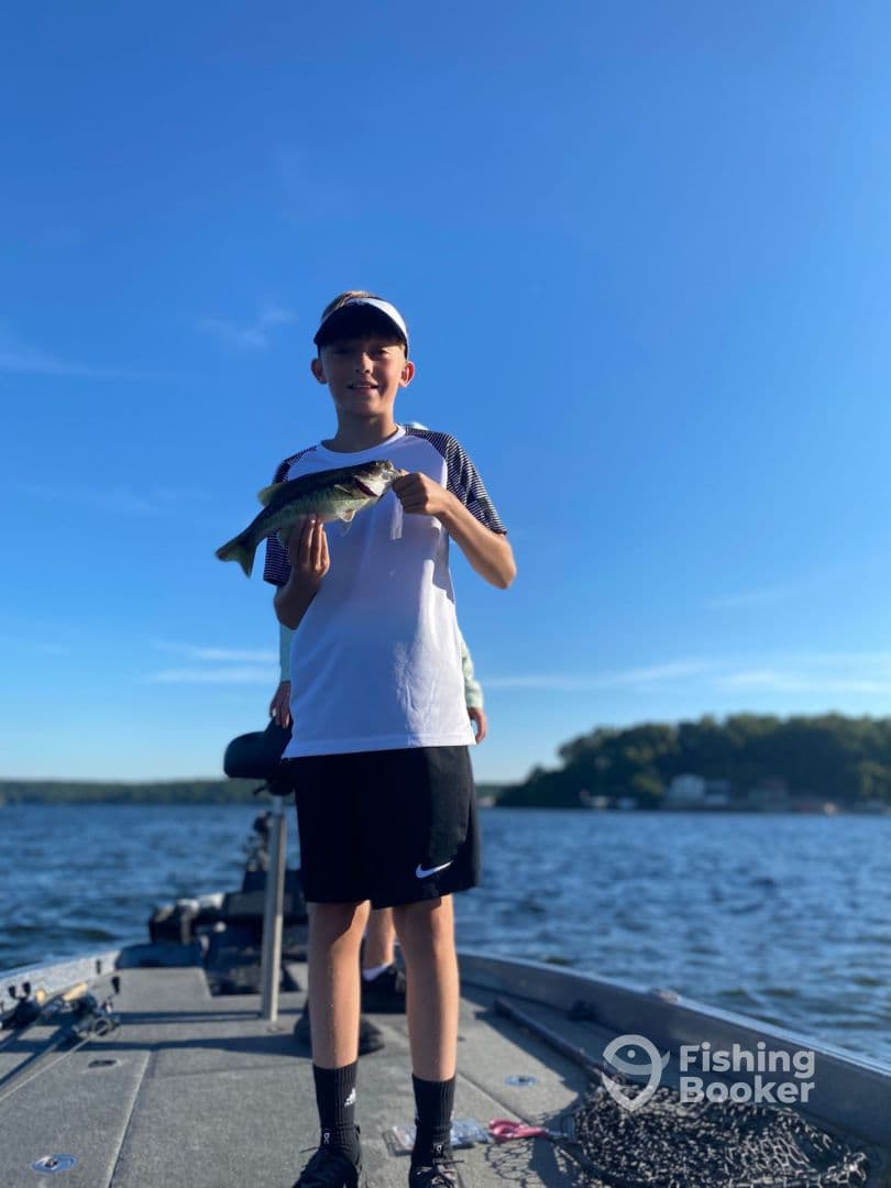 A young angler proudly displaying a Largemouth Bass while fishing on a sunny day, showcasing a vibrant lake backdrop.