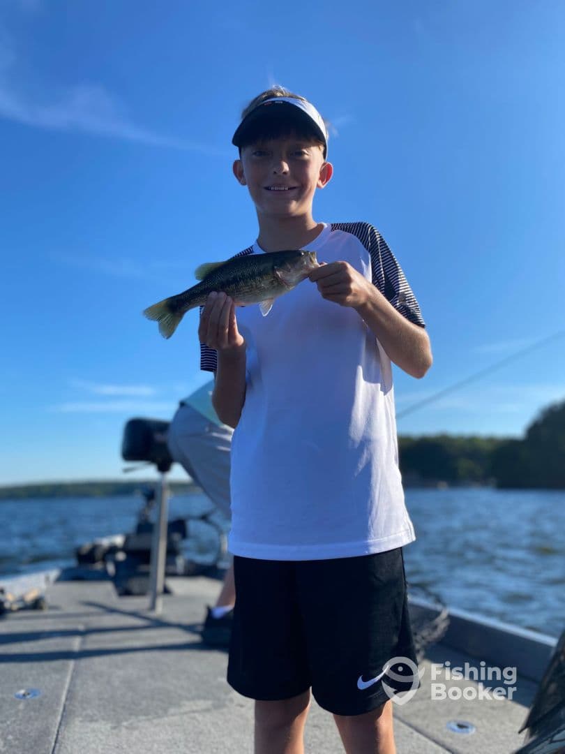 A young angler proudly displaying a Largemouth Bass while fishing on a sunny day.