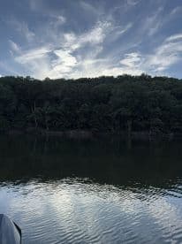 A scenic view of a calm lake surrounded by lush greenery and a dramatic sky, ideal for a peaceful fishing experience.
