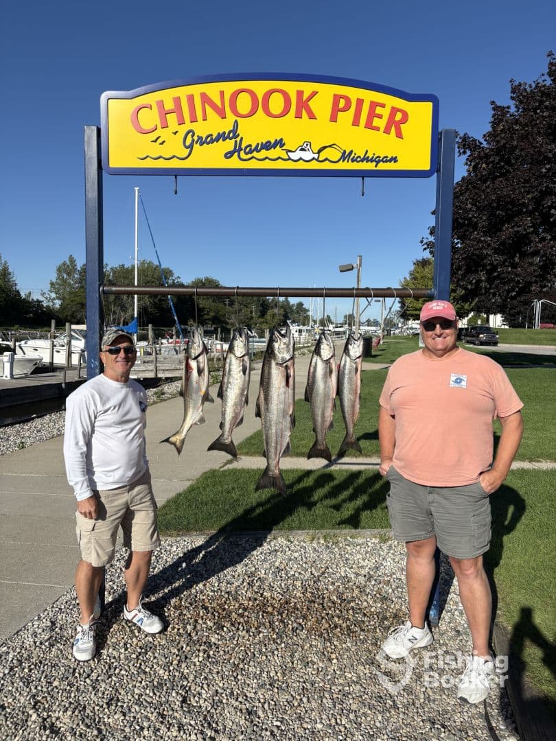 Two anglers proudly displaying a catch of salmon on a board at Chinook Pier in Grand Haven, Michigan.