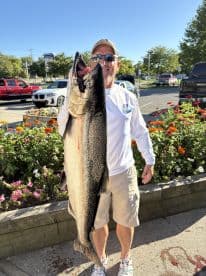An angler proudly displaying a large Chinook Salmon in a vibrant outdoor setting, showcasing a successful fishing trip.