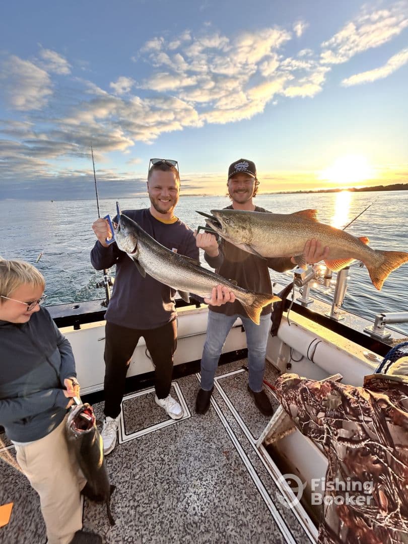 Two anglers proudly displaying their catch of large Lake Trout aboard a fishing boat during a sunset outing.