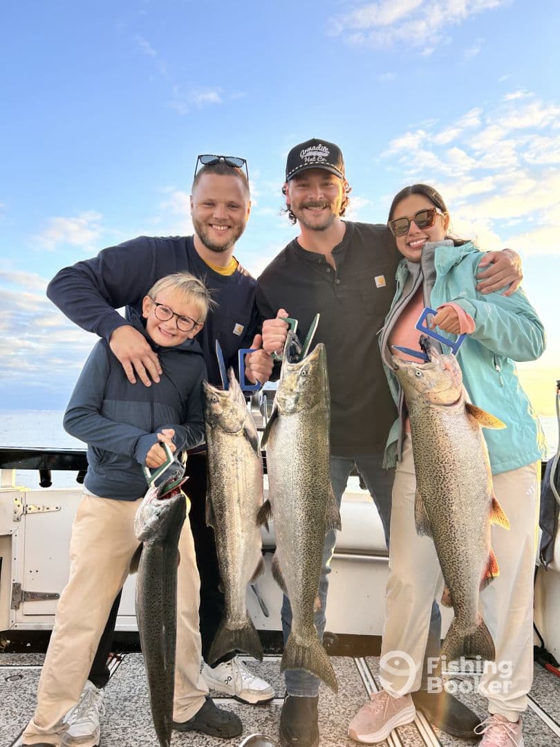 A family proudly displaying their catch of large Lake Trout while enjoying a fishing trip on a boat.
