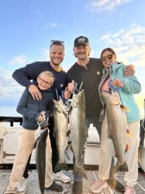 A family proudly displaying their catch of large Lake Trout while enjoying a fishing trip on a boat.