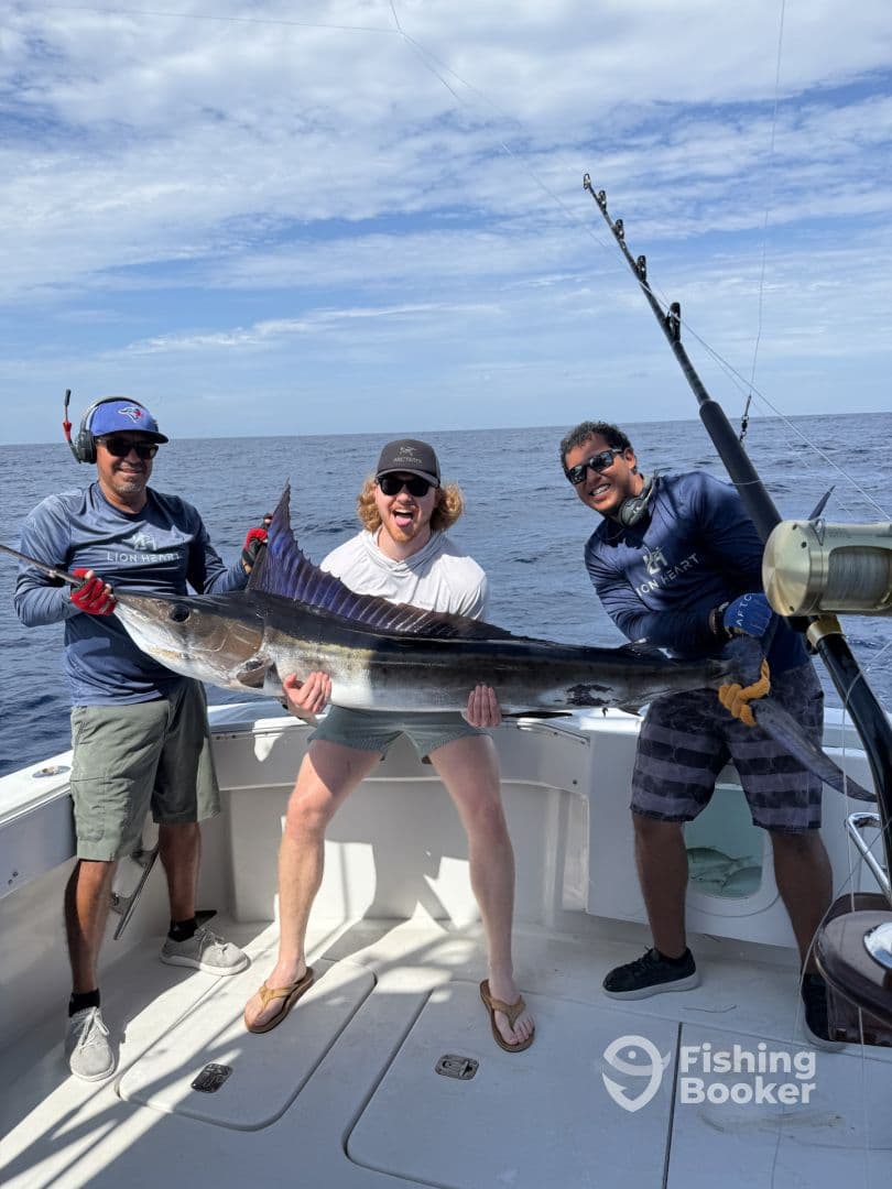 Three anglers proudly displaying a large Sailfish aboard a sportfishing boat, showcasing their successful catch during a deep-sea fishing trip.