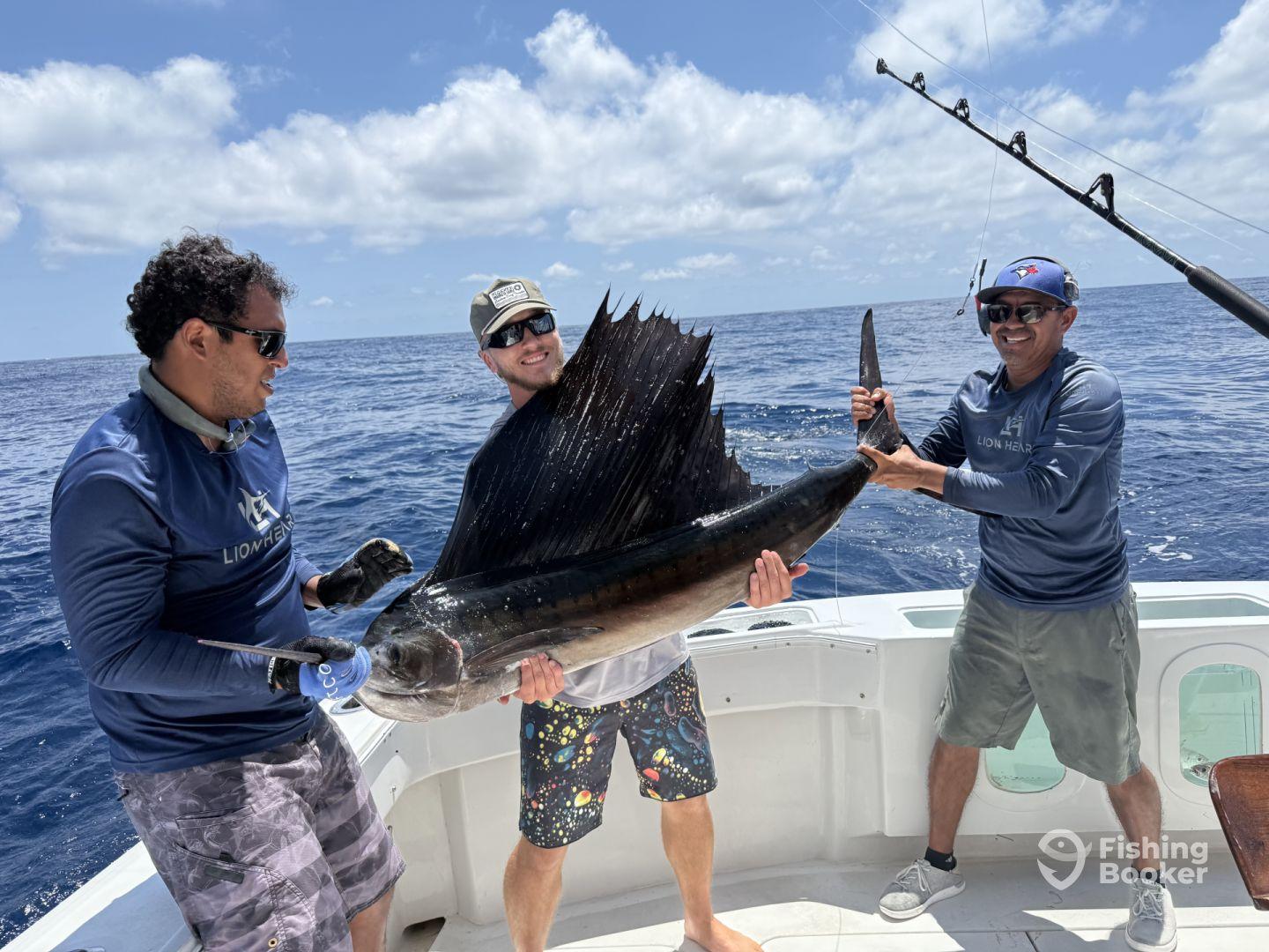 Three anglers proudly displaying a large Sailfish aboard a sport fishing boat in open waters.