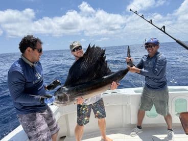 Three anglers proudly displaying a large Sailfish aboard a sport fishing boat in open waters.