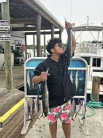 A young angler joyfully displaying a large fish alongside a catch of smaller fish at the dock, showcasing a successful fishing trip.