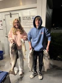 Two young anglers proudly displaying their catch of large Lake Trout after a successful fishing trip.