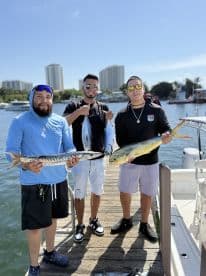 Three anglers proudly displaying their catch of a Mahi Mahi and a Barracuda while docked at a waterfront location.