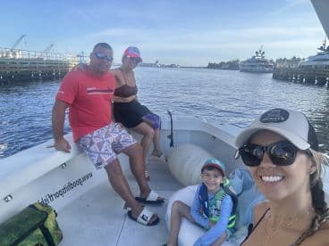 A family enjoying a day on a boat, with a young boy wearing a life jacket and smiling at the camera, while adults relax in the background.