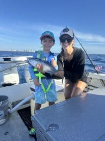 A young boy and an adult female proudly displaying a caught fish while on a boat, enjoying a sunny day on the water.