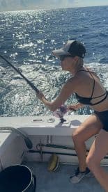 A female angler actively reeling in a catch while fishing on a sunny day at sea, showcasing the excitement of deep-sea fishing.