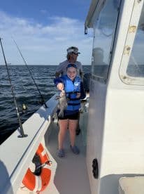 A young angler proudly displaying a Black Sea Bass while fishing on a boat, enjoying a sunny day on the water.