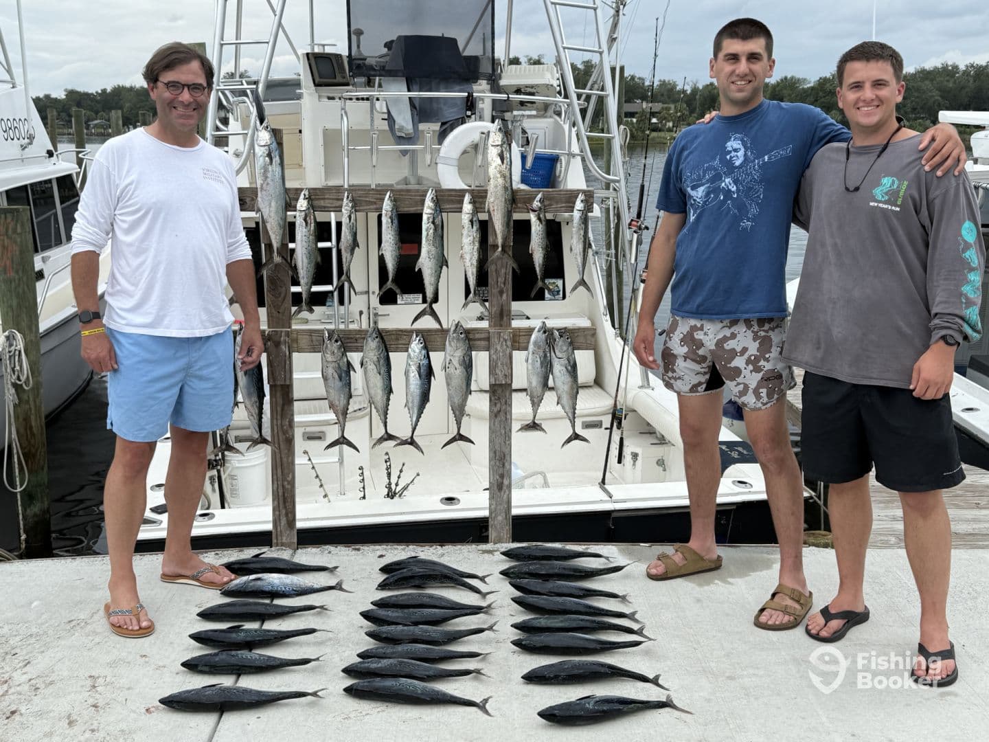 Three anglers proudly displaying their catch of multiple fish, including Mackerel, arranged on a board at the dock after a successful fishing trip.