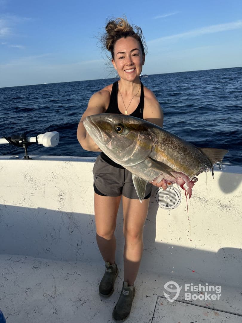 An angler proudly displaying a large Amberjack caught during a deep-sea fishing trip.