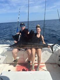Two anglers proudly displaying a large Sailfish aboard a sport fishing boat in open water.