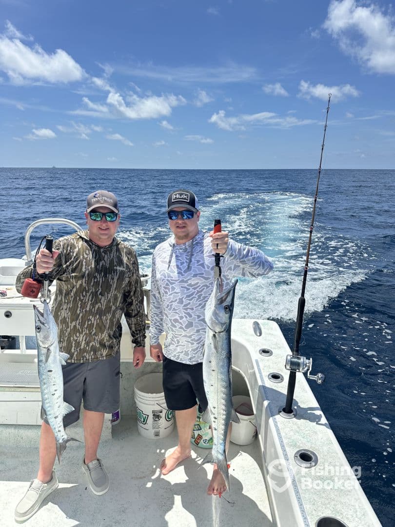 Two anglers proudly displaying their catch of Barracuda while fishing offshore, showcasing a sunny day on the water.