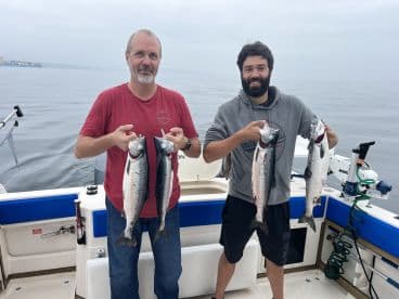 Two anglers proudly displaying their catch of Salmon while fishing on a boat in calm waters.