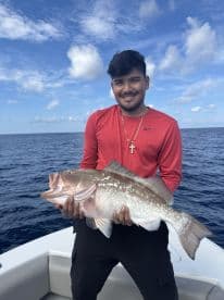 A young angler proudly displaying a large Grouper while fishing offshore, showcasing a beautiful day on the water.