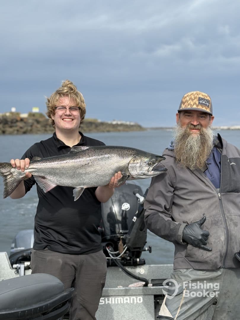 A young angler and an adult proudly displaying a large Salmon while fishing from a boat, showcasing a successful day on the water.