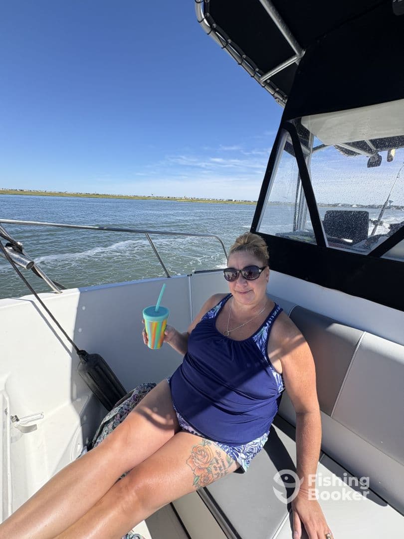 A woman relaxing inside a boat, enjoying a drink while cruising on calm waters, showcasing a comfortable seating area.