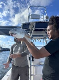 Two anglers on a boat celebrating a successful catch of a Redfish, showcasing the excitement of a day on the water.