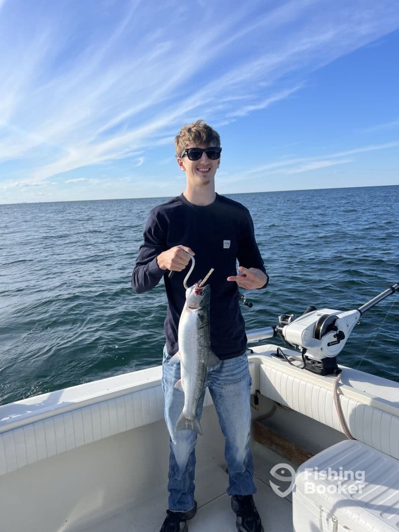 A young angler proudly displaying a large Salmon while fishing on a boat in open waters.